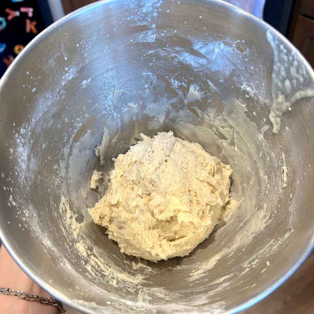 A metal mixing bowl containing a ball of cookie dough, with some dough sticking to the sides.