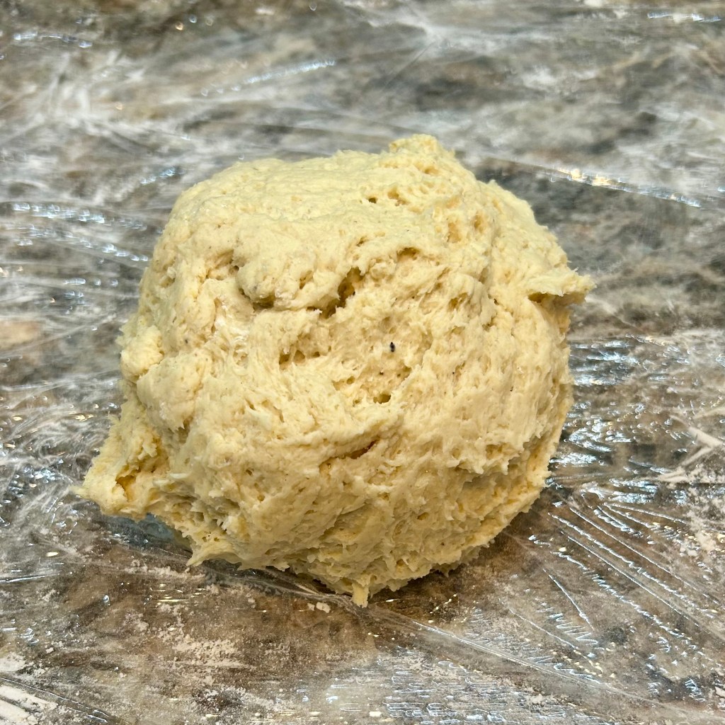 A ball of dough on a kitchen countertop covered with plastic wrap.