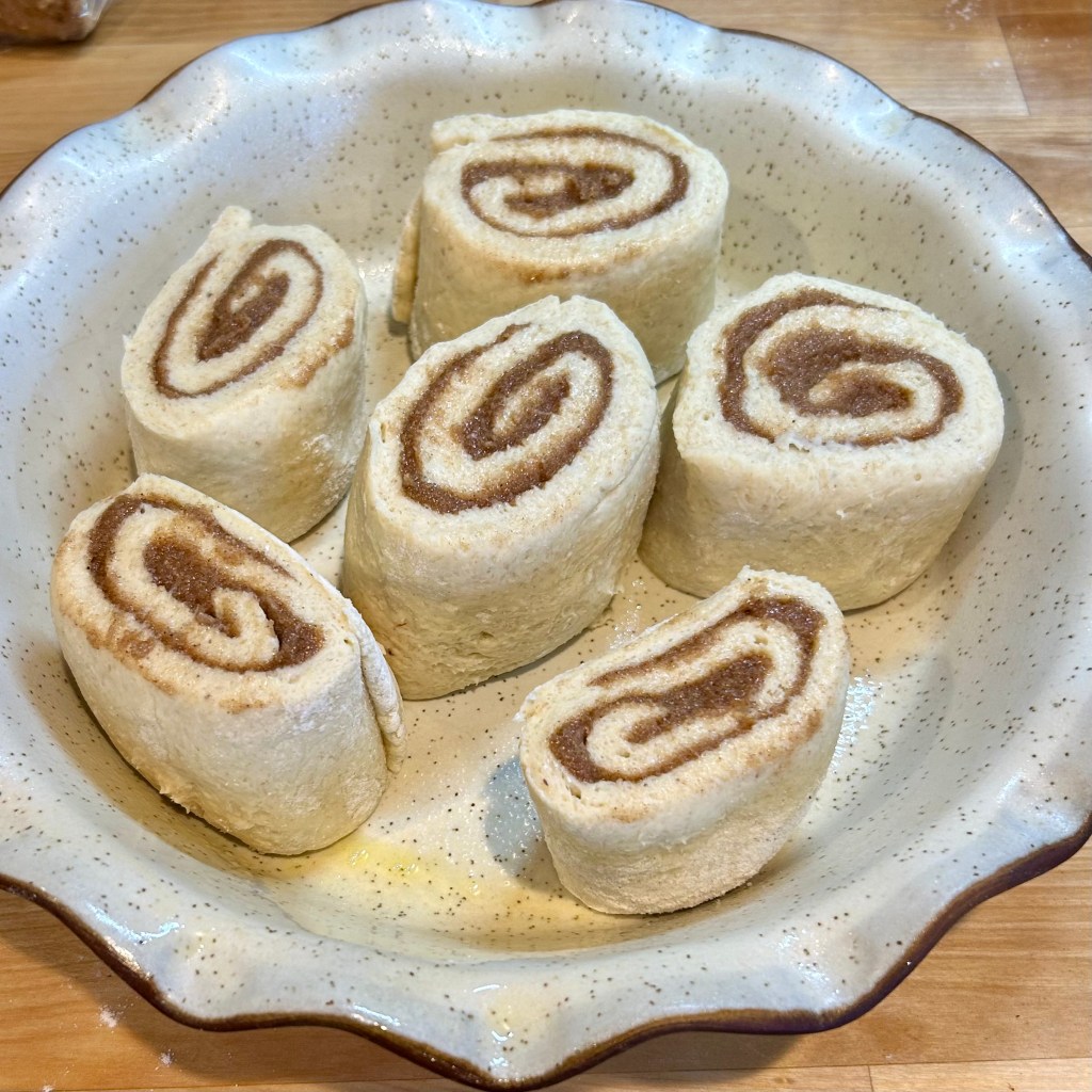 A dish containing several uncooked cinnamon rolls arranged neatly in a round, speckled baking dish.