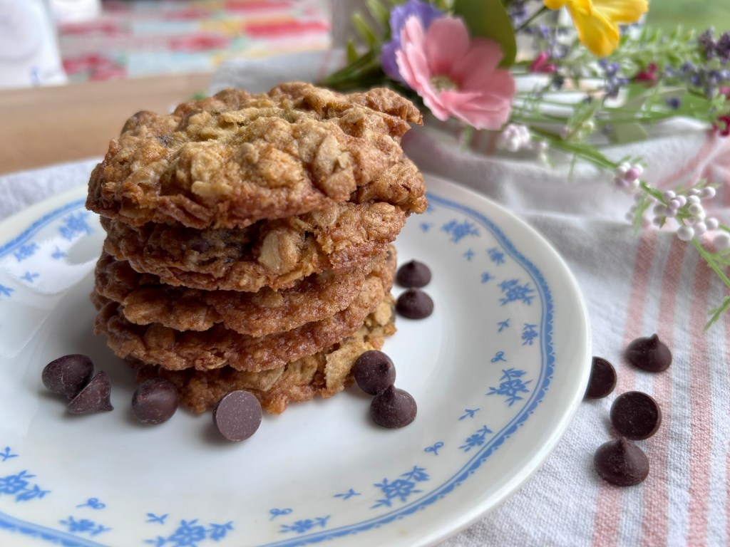 A plate with a stack of oatmeal cookies and chocolate chips, surrounded by small flowers.